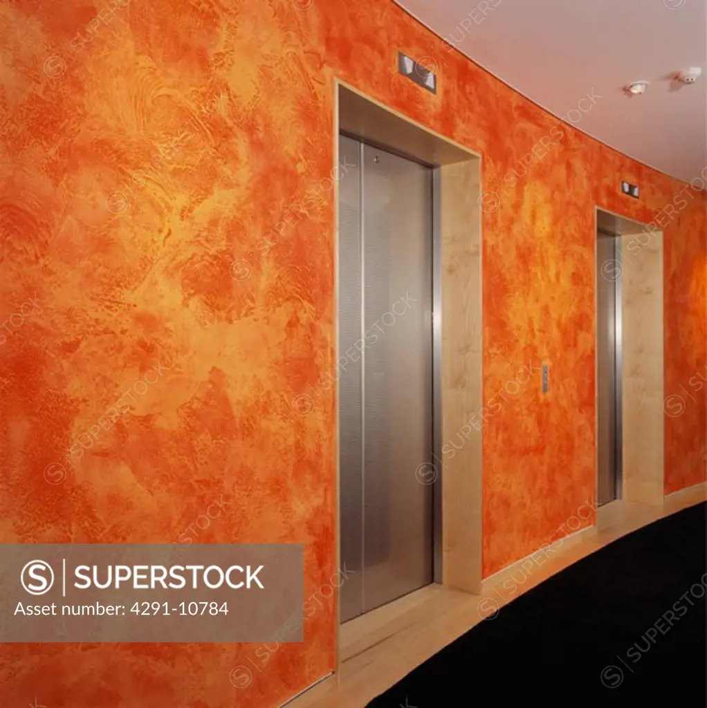 Stainless steel doors on lift in lobby of hotel with orange-red spongeing effect on walls