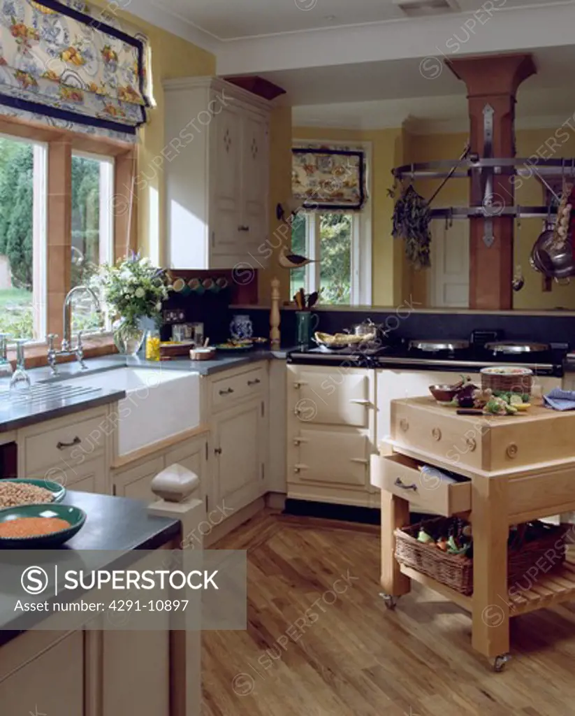 Patterned blind above white ceramic sink in cottage kitchen with cream aga and wooden flooring