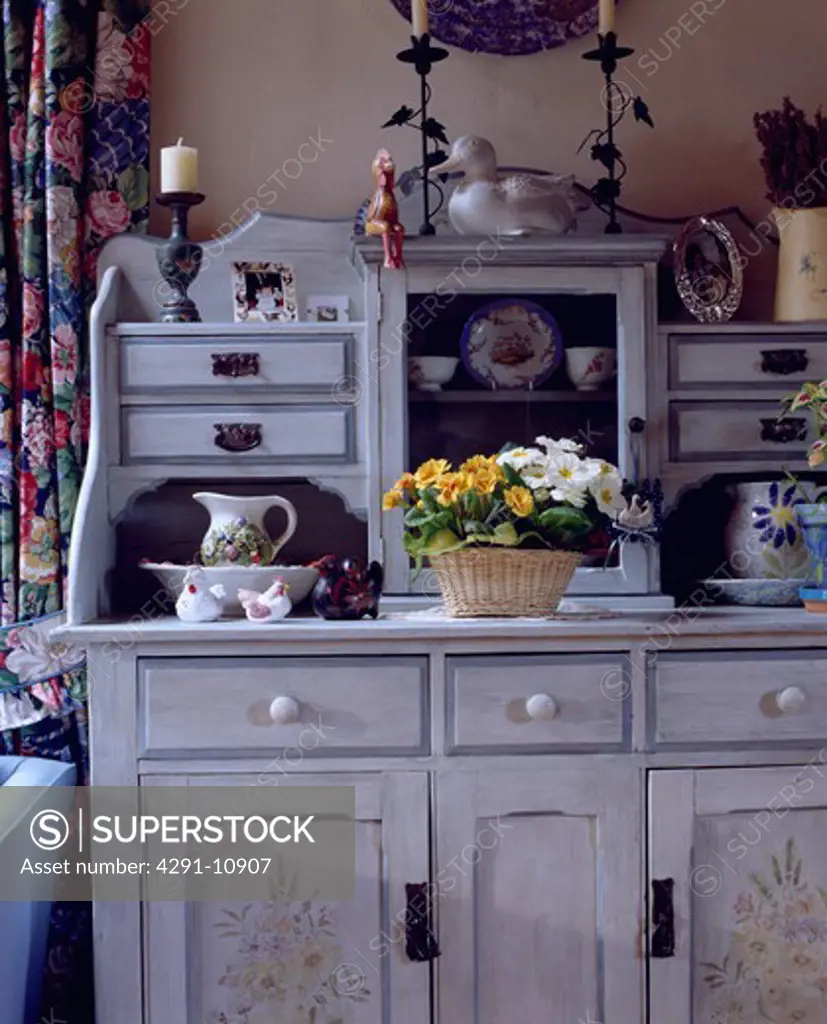 Basket of primulas on paint grey dresser with floral stencilling