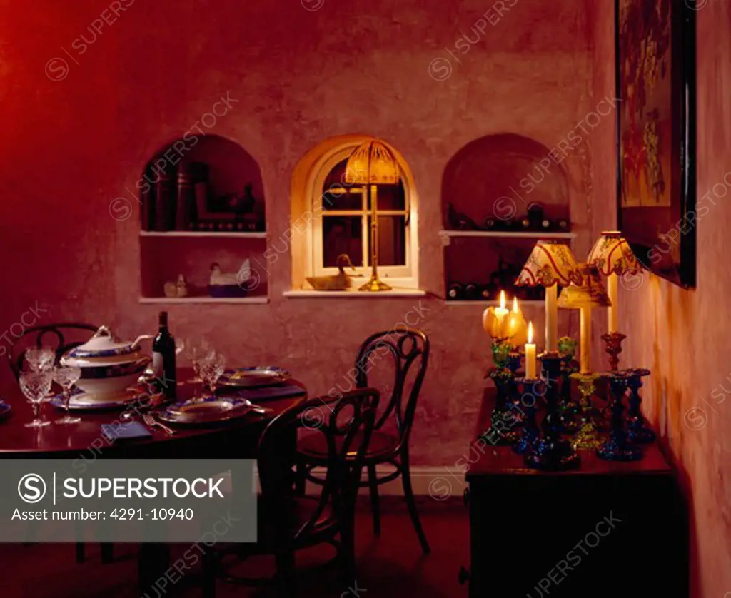 Lighted lamp in small arched window between arched alcoves in red dining room with lighted candles