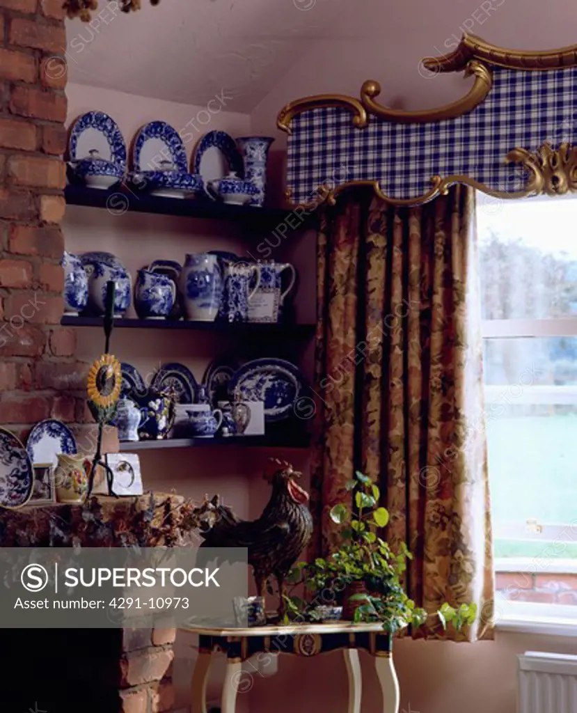 Blue and white jugs on shelves beside window with gilt-edged blue and white checked pelmet and floral curtains