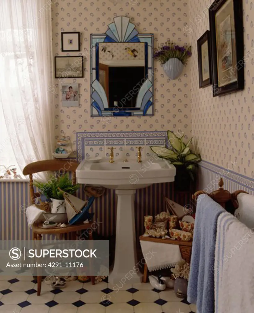 Blue stained glass mirror above pedestal basin in seaside themed bathroom with blue and white wallpaper and dado