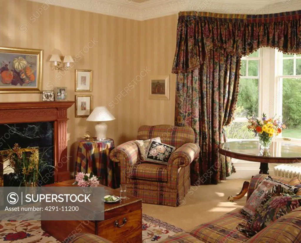 Armchair beside fireplace in traditional living room with striped wallpaper and dark floral curtains