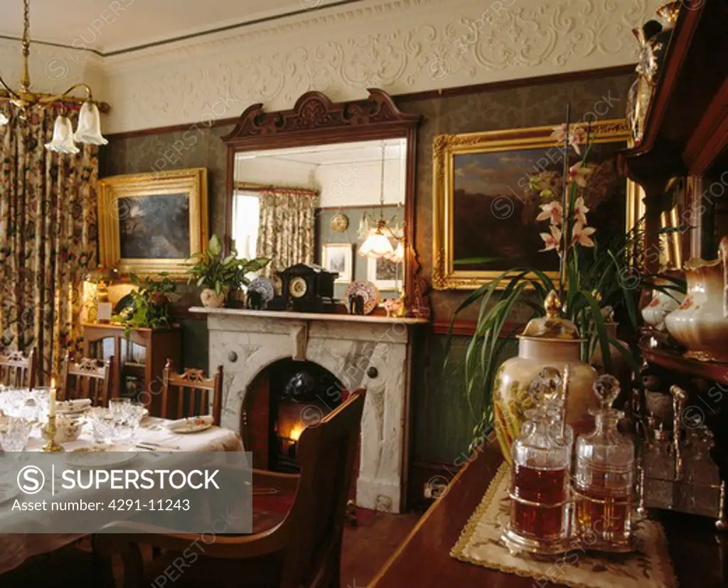 Mirror above fireplace in Victorian dining room with gilt-framed pictures and ornate plasterwork cornice