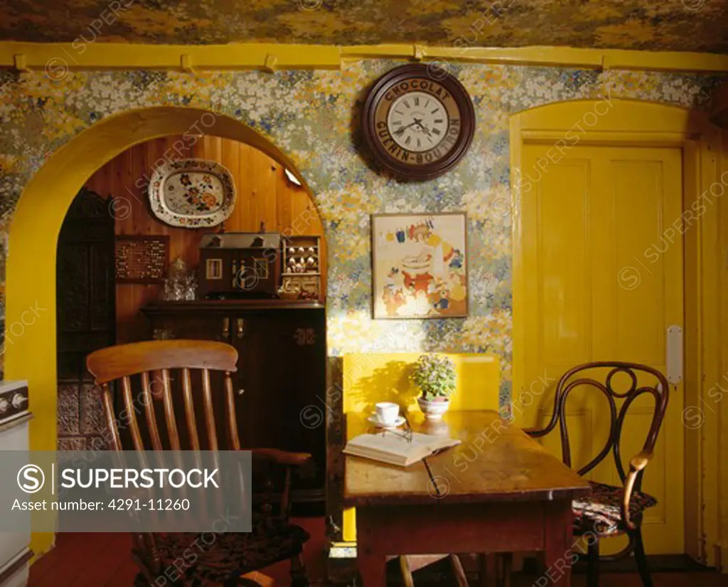 Windsor and Bentwood chairs at wooden table in dining room with floral wallpaper and yellow paintwork