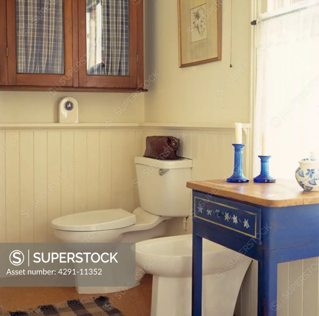 Small painted blue table beside bidet and toilet in cream bathroom with panelling to dado height
