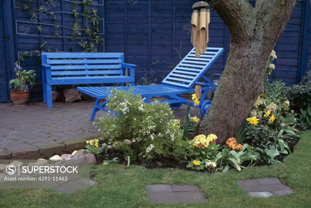 Bluepainted patio furniture with a spring border of polyanthus and daffodils around the base of a tree.