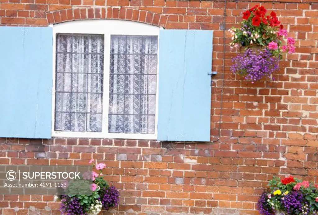 Pastel blue shutters on cottage window with flowering plants in hanging baskets