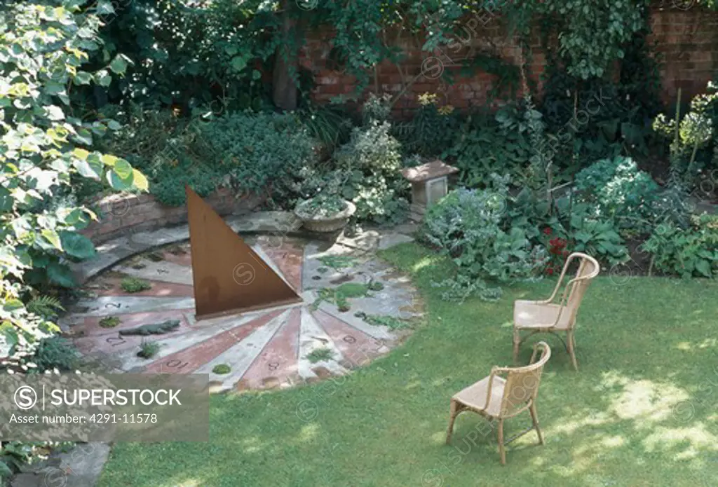 Wicker chairs on lawn beside circular paved patio with triangular metal sculpture