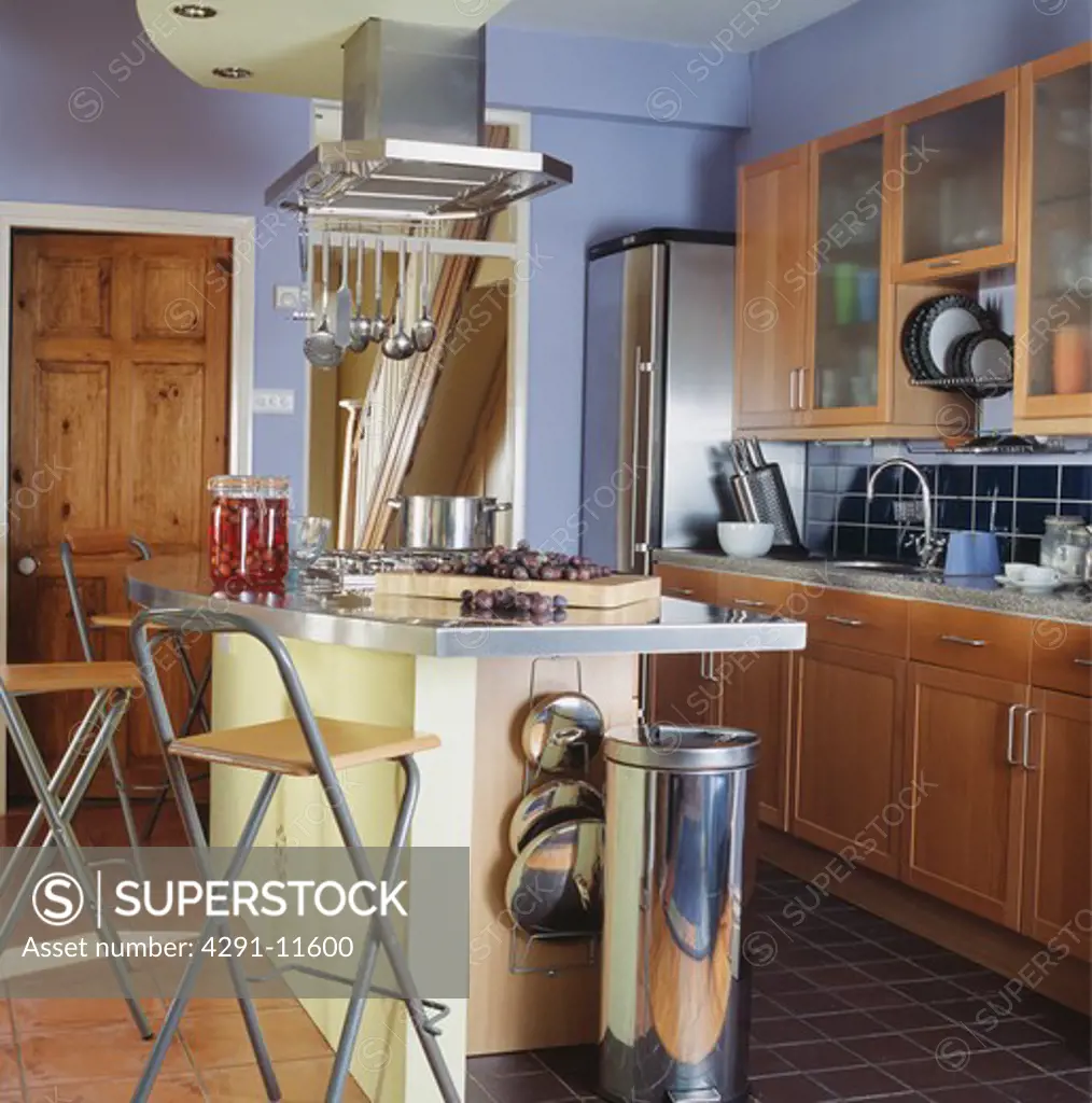 Steel waste bin below breakfast bar on island unit with metal and wood stools in blue country kitchen