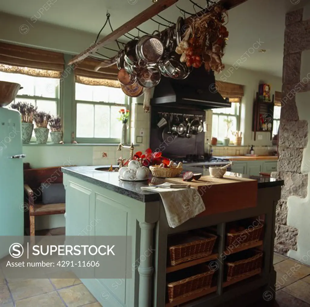 Pans on storage rack above grey-green island unit in cottage kitchen