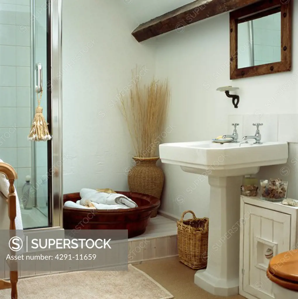 White pedestal basin in country bathroom with towels in large wooden bowl beside shower