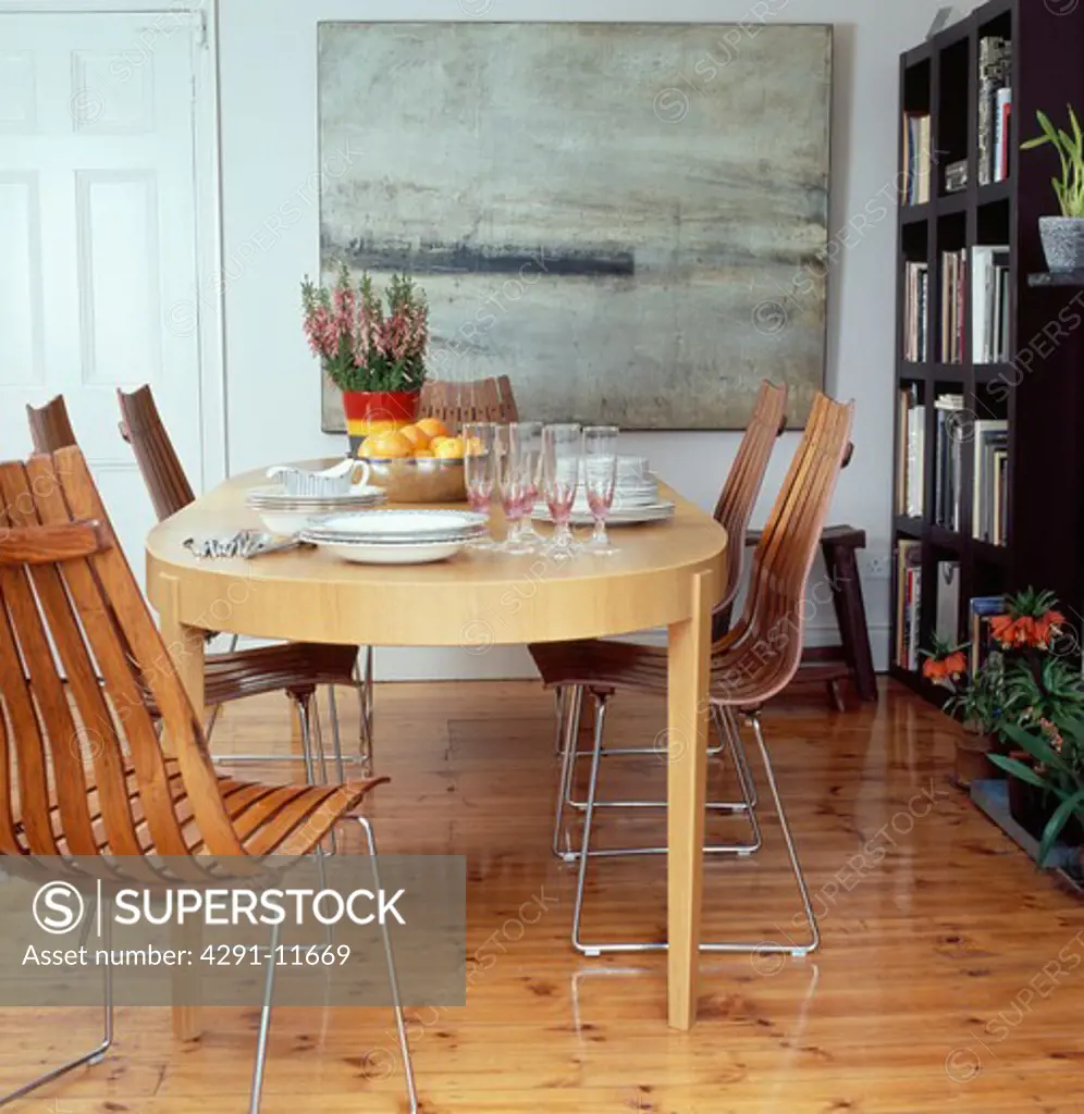 Modern wooden table and chairs in dining room with large painting and wooden flooring