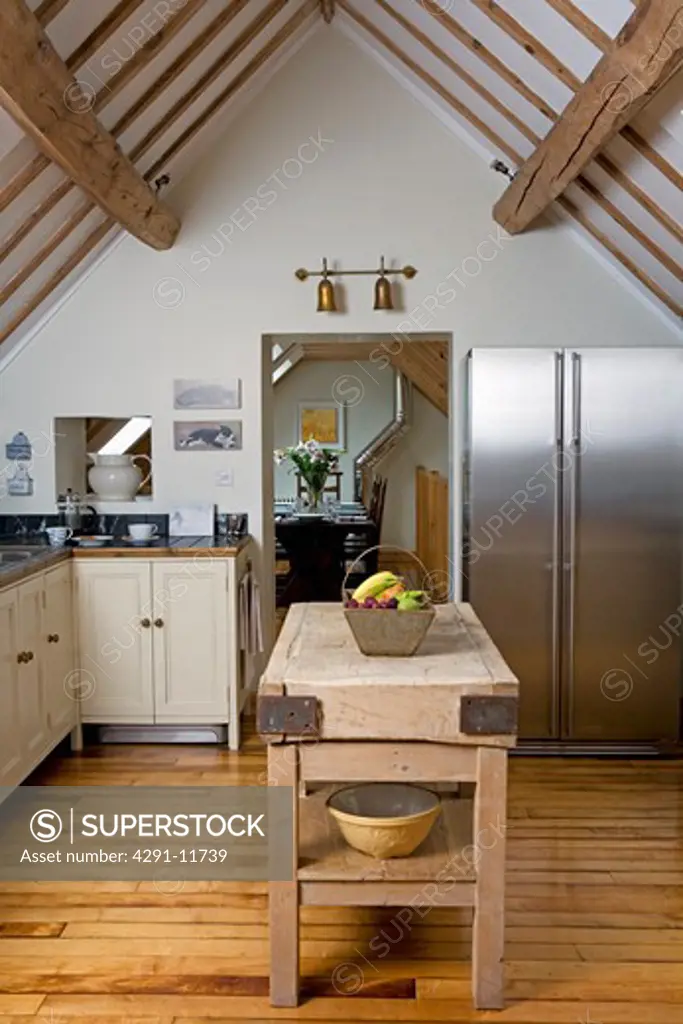 Old butchers block on wooden floorboards in modern country kitchen with American style fridge freezer and apex ceiling