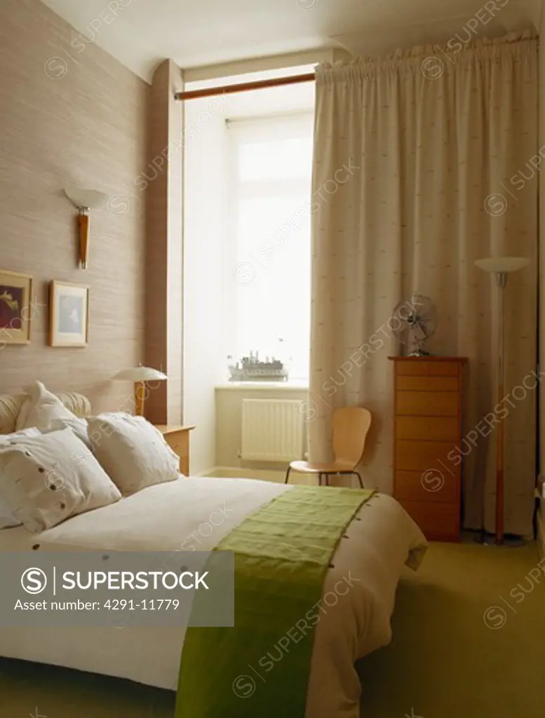 Green throw on bed with white pillows and quilt in modern bedroom with cream curtains