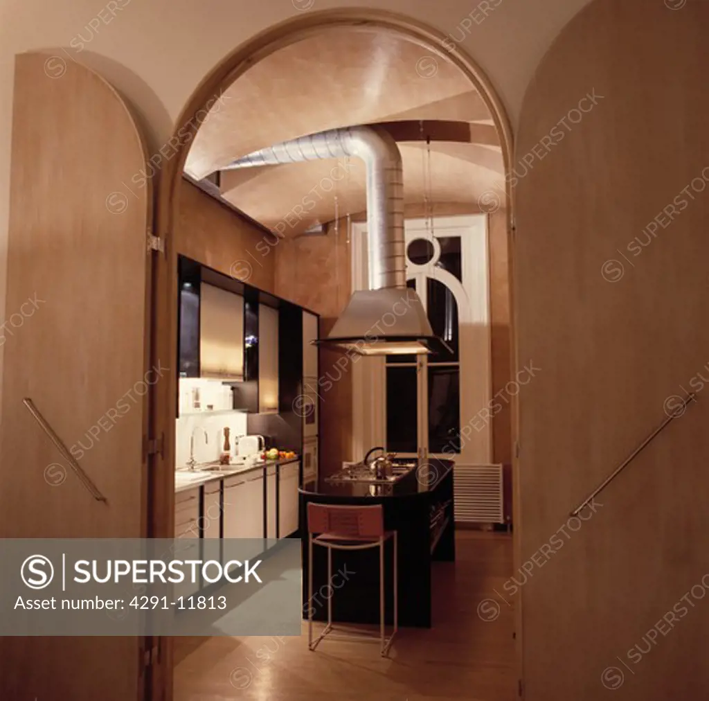 Large wood double doors on arched doorway to modern townhouse kitchen with steel extractor above island unit