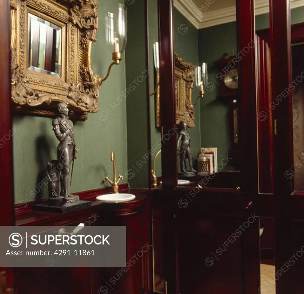 Bronze statue on shelf above small corner basin in green cloakroom with mahogany panelling