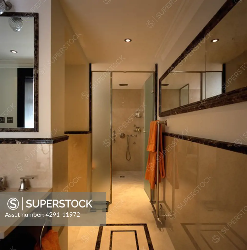 Long mirror in travertine-tiled modern bathroom with opaque glass doors open to wet room shower