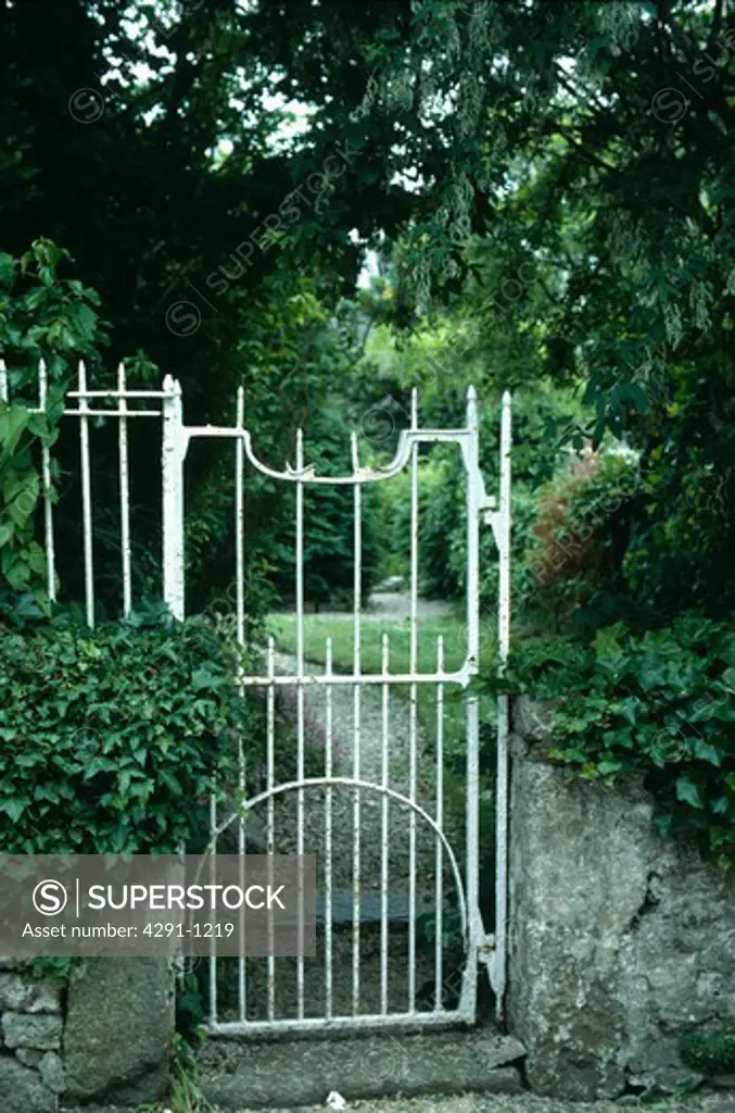 White iron garden gate with view of path through country garden