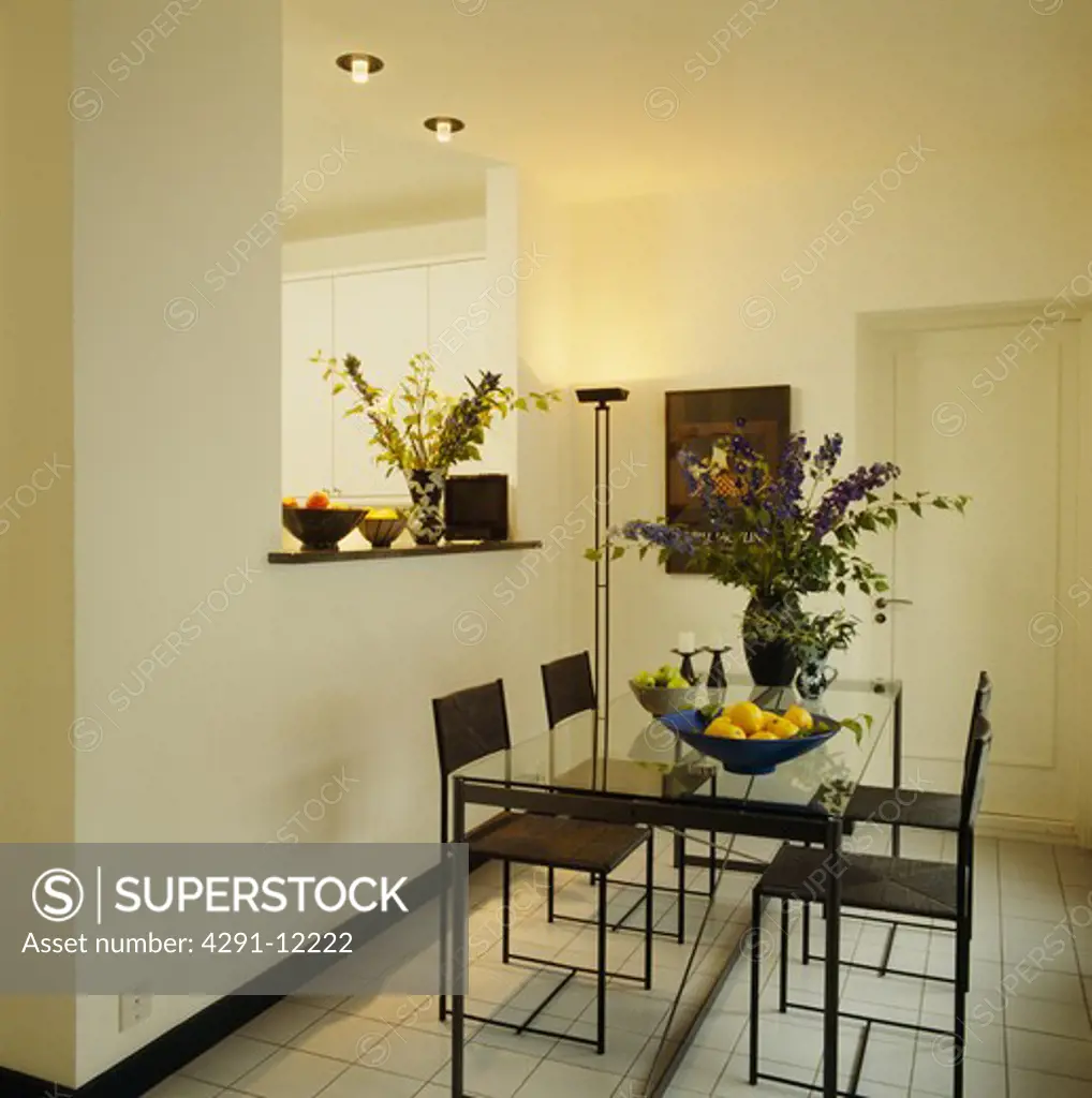 Black metal chairs and glass-topped table in modern white dining room with uplighter and recessed lighting