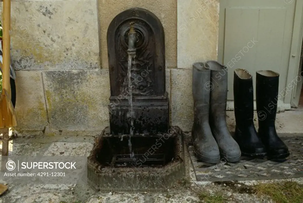 Close-up of black wellington boots and running tap