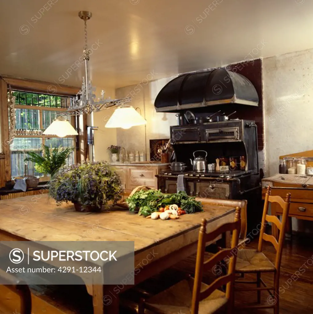 Double pendant light above large pine table with ladderback chairs in kitchen with extractor above black range oven