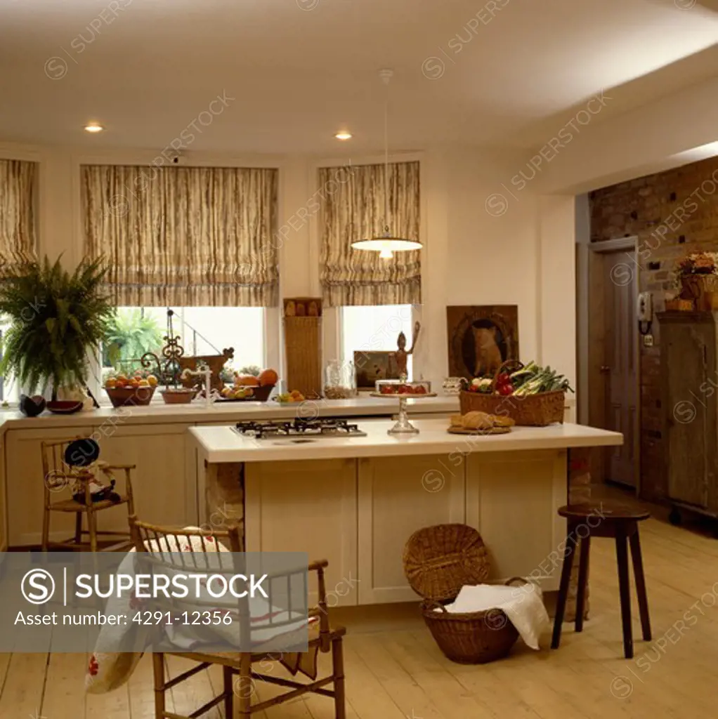 Patterned blinds in cream kitchen with antique chairs and wooden stool beside rectangular island unit
