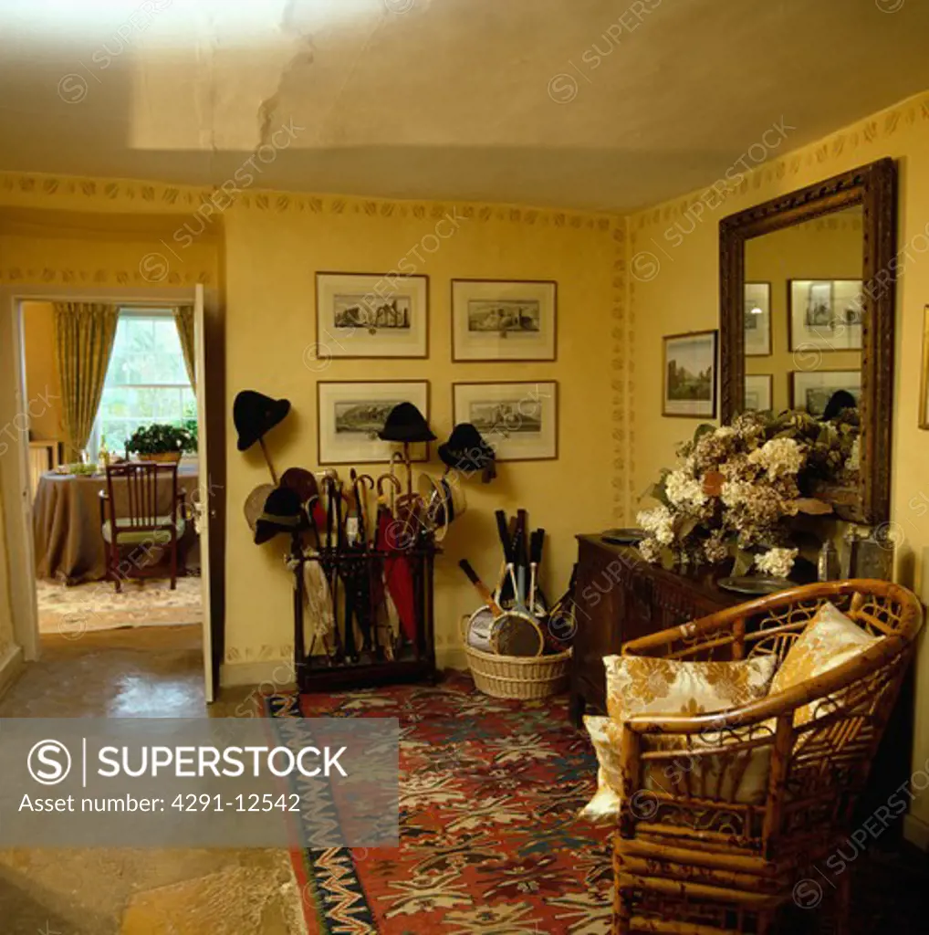 Oriental rug and cane chair in yellow country hall with umbrellas and sticks in umbrella stand