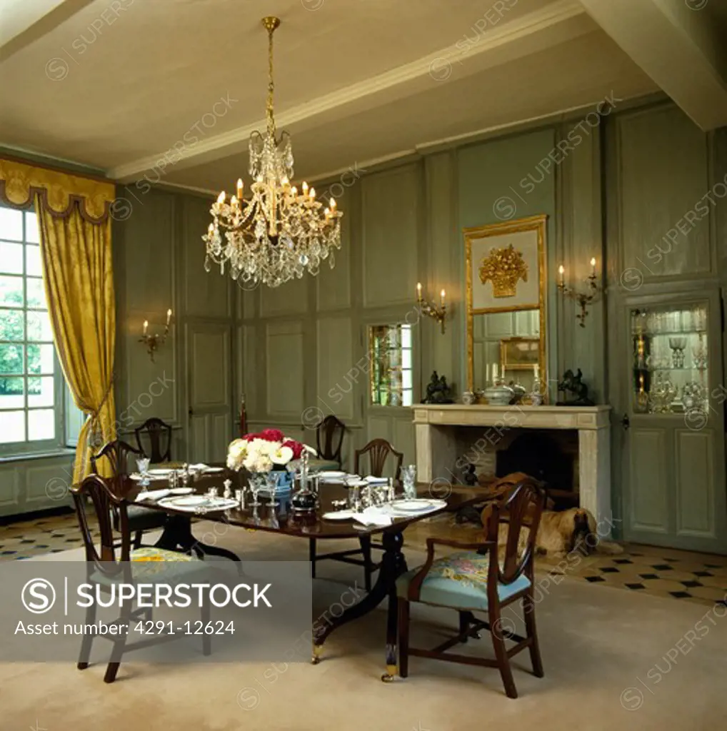 Antique crystal chandelier above antique table and chairs in green panelled country dining room with cream carpet