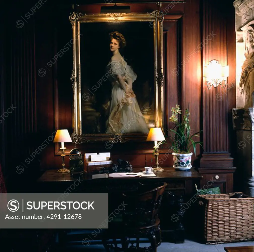 Large Edwardian portrait above table with lighted lamps in panelled study