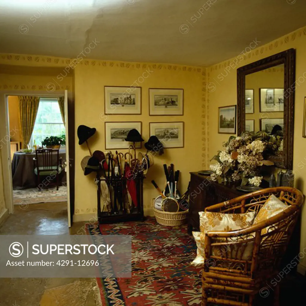Oriental rug and cane chair in yellow country hall with umbrellas and sticks in umbrella stand