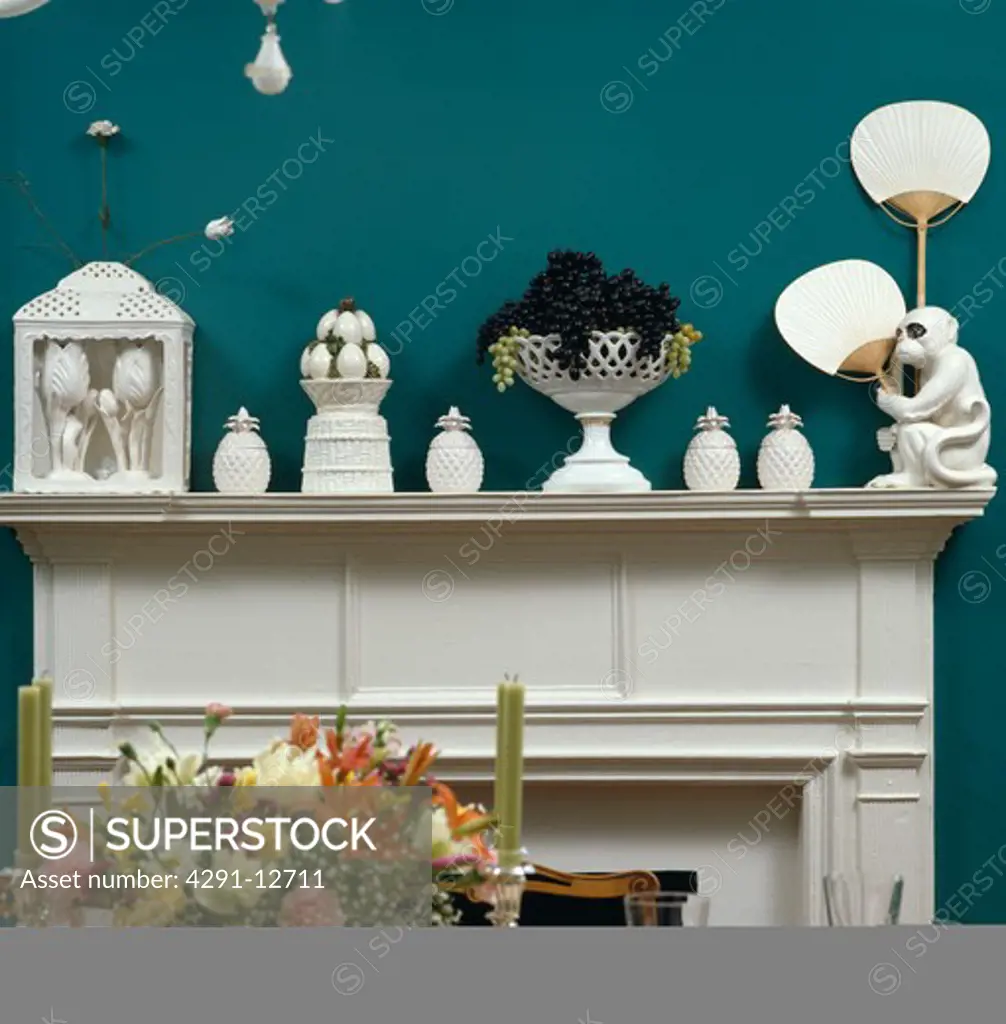 Collection of white china ornaments on white mantelpiece in dark blue dining room with vase of flowers on table