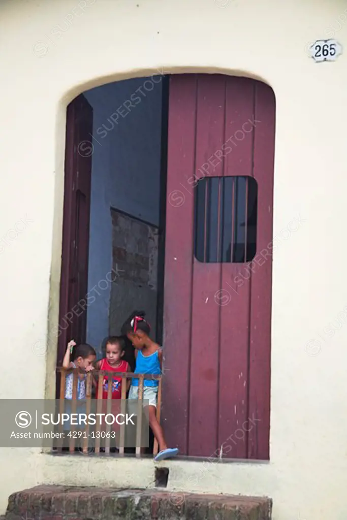 Three young children in large doorway, behind protective safety barrier, Camaguey, Camaguey Province, Cuba