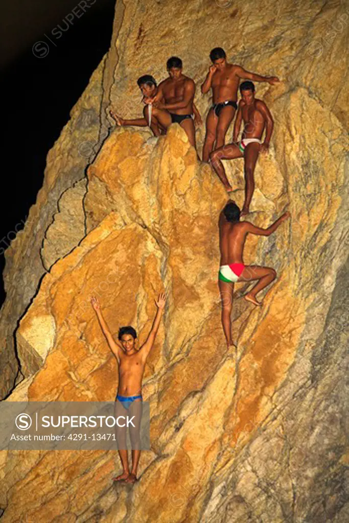 Cliff divers on cliff face at night before diving at La Quebrada, Mexico