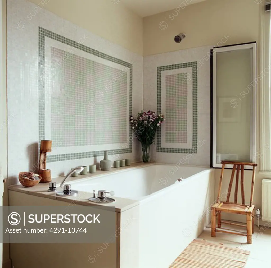 Mosaic tiled wall above bath in traditional bathroom with bamboo chair in front of folding glass panel