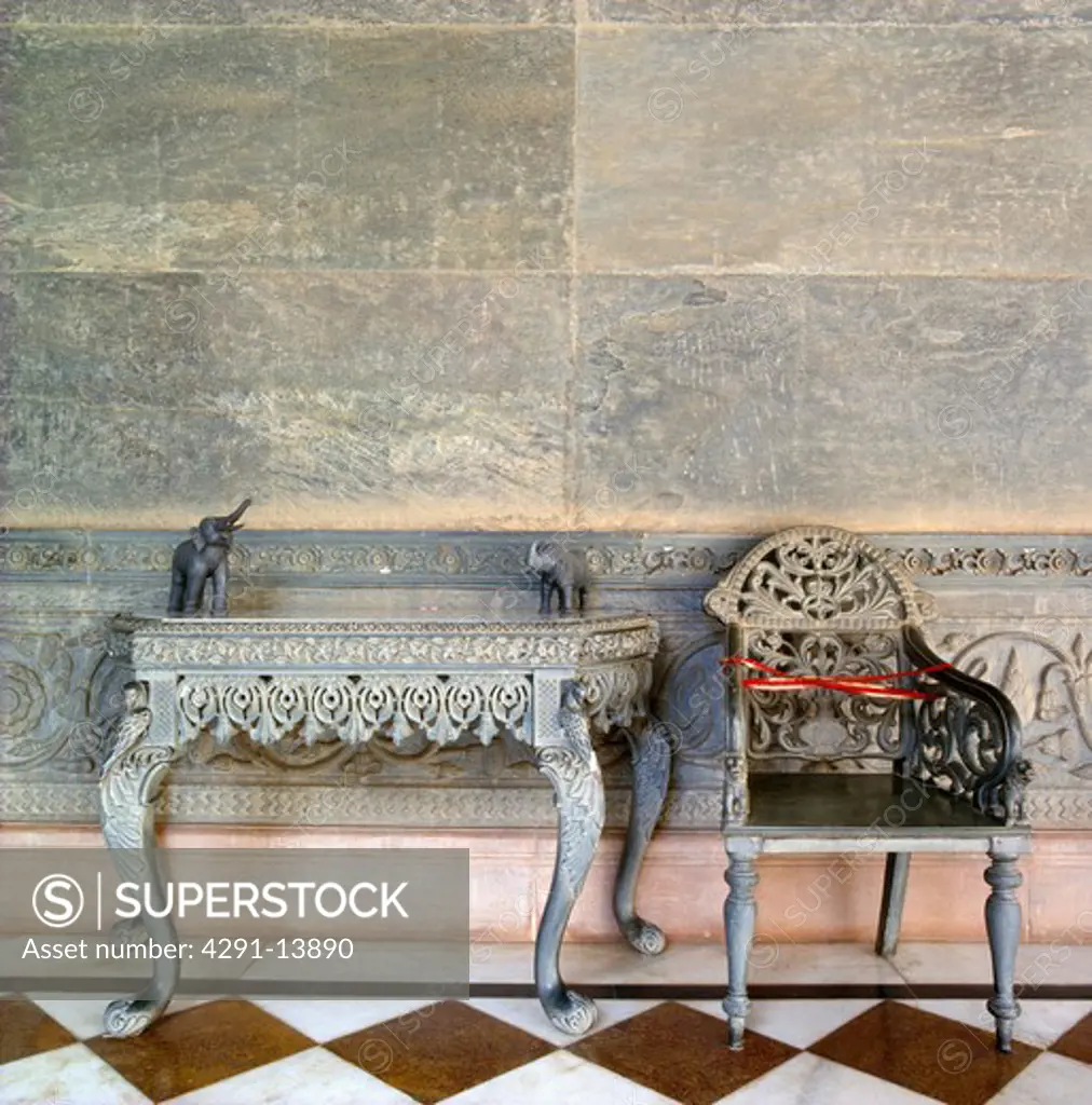 Close-up of intricately carved old Rajastani table and chair against tiled wall