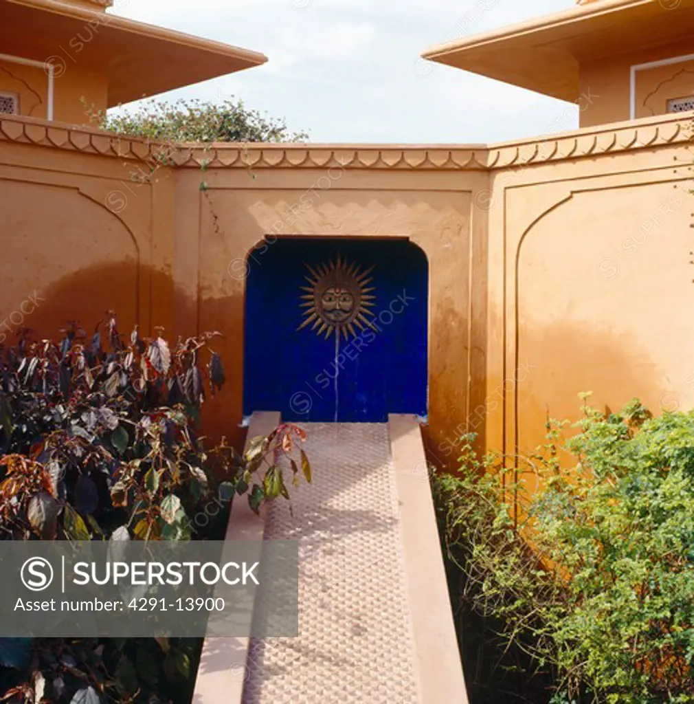 Narrow marble bridge to Indian sculpture in blue tiled alcove in sandstone courtyard in Rajastan