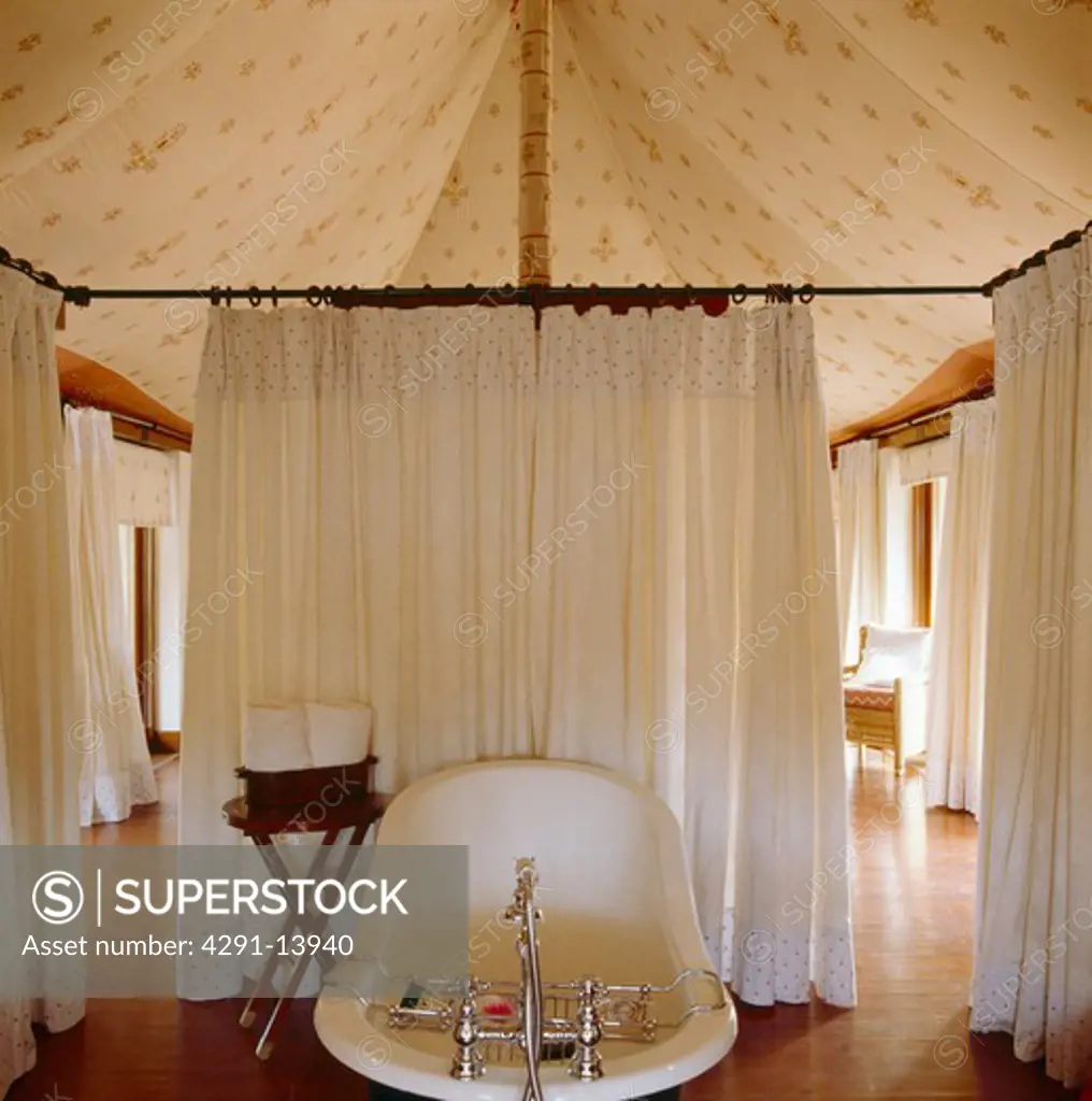 Rolltop bath and white linen curtains in bathroom in Rajastani tent with wooden flooring