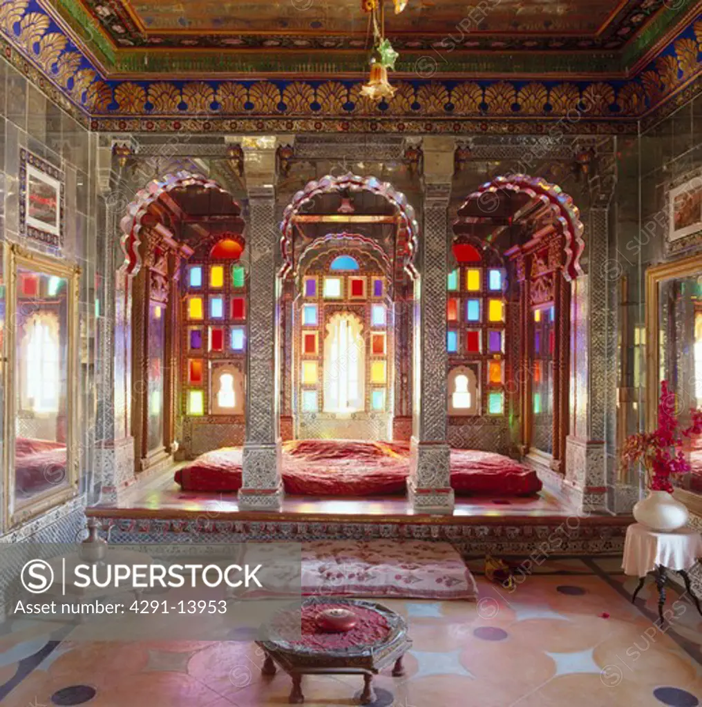 Intricately painted walls and arches in Rajastani bedroom with stained glass windows at the Deogarh Mahal hotel