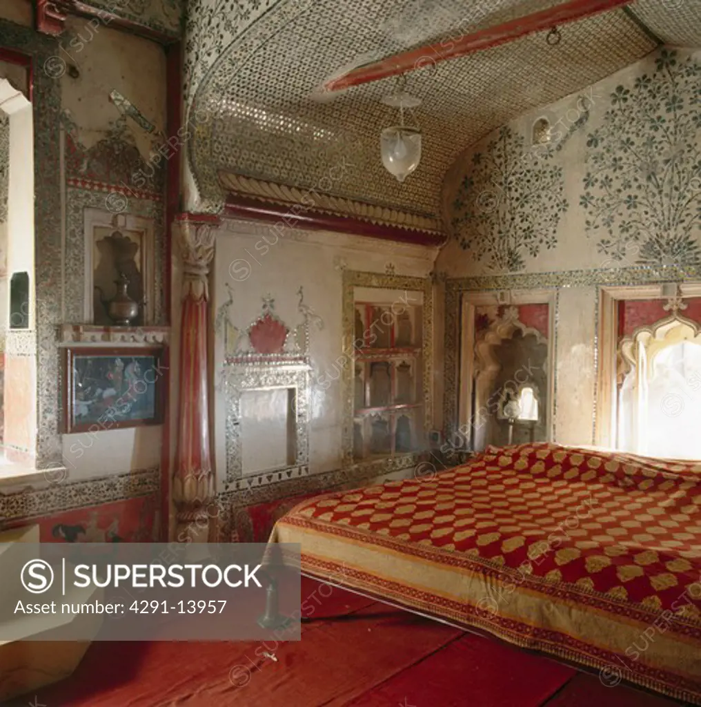 Red and yellow Indian bedcover on bed in Rajastani bedroom with floral mosaic tiled walls and ceiling