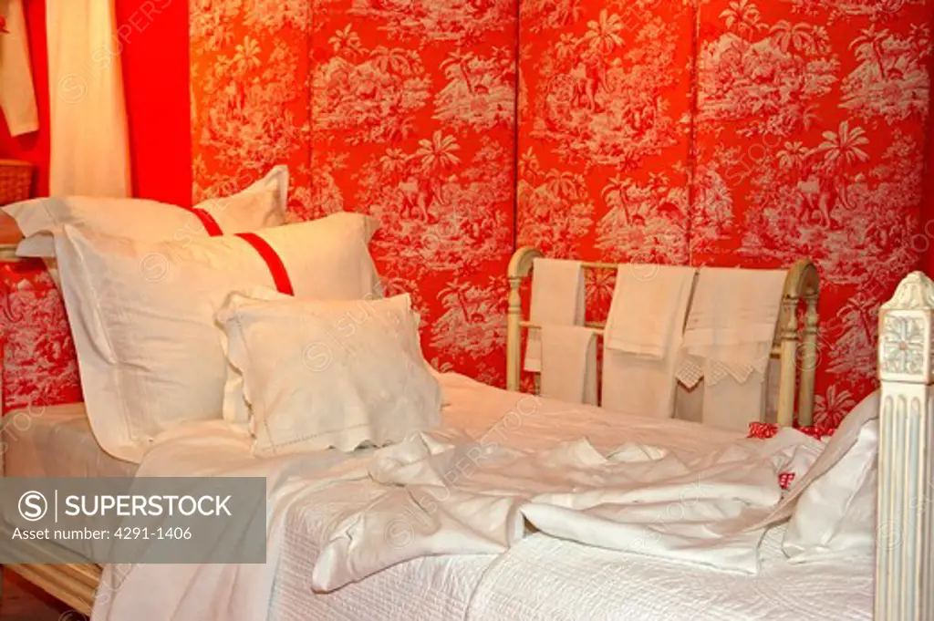 Close-up of bed with white linen and pillows against orange toile-de-jouy folding screen