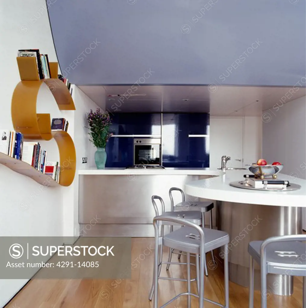 Metal chairs and steel breakfast bar with white worktop in modern kitchen diningroom with Arad Bookwork shelf on wall