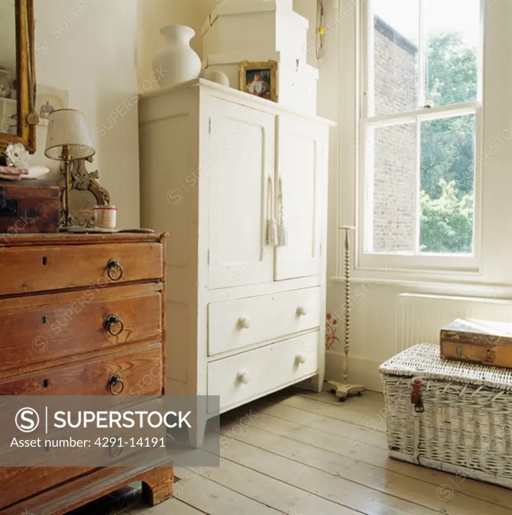 Cream painted linen press and antique chest-of-drawers in front of sash window