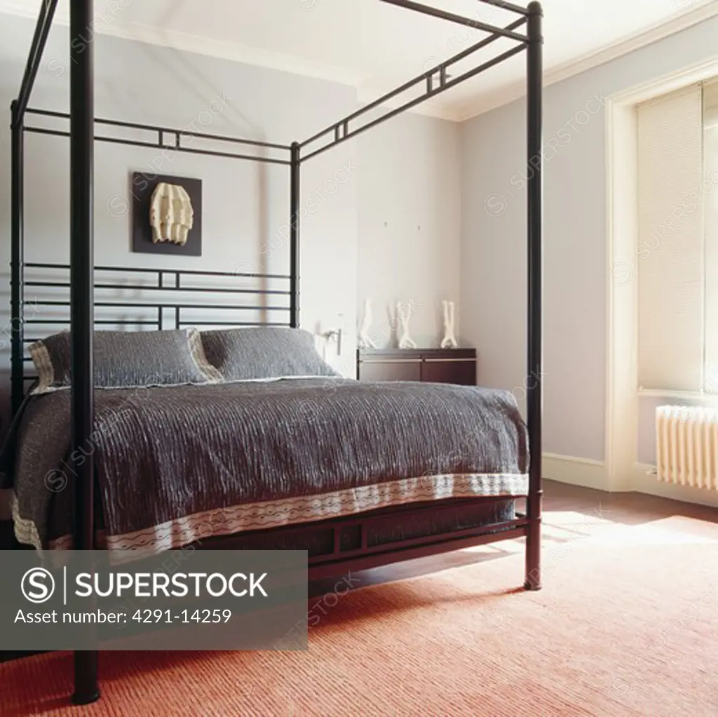 Modern black metal four-poster bed with charcoal grey bedcover and cushions in pale grey bedroom