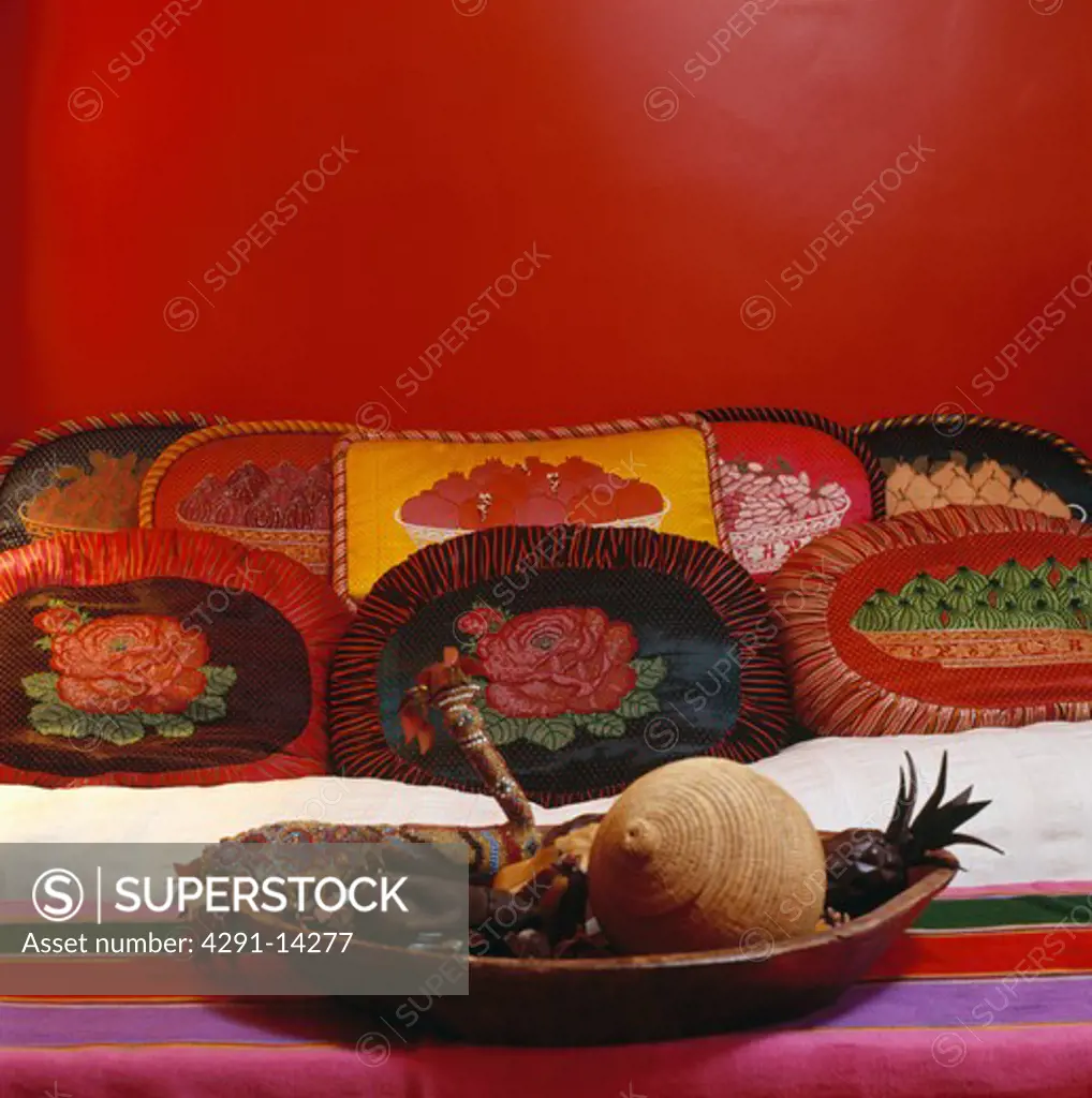Colourful cushions on cream sofa in red Middle Eastern style living room with wooden bowl on striped tablecloth
