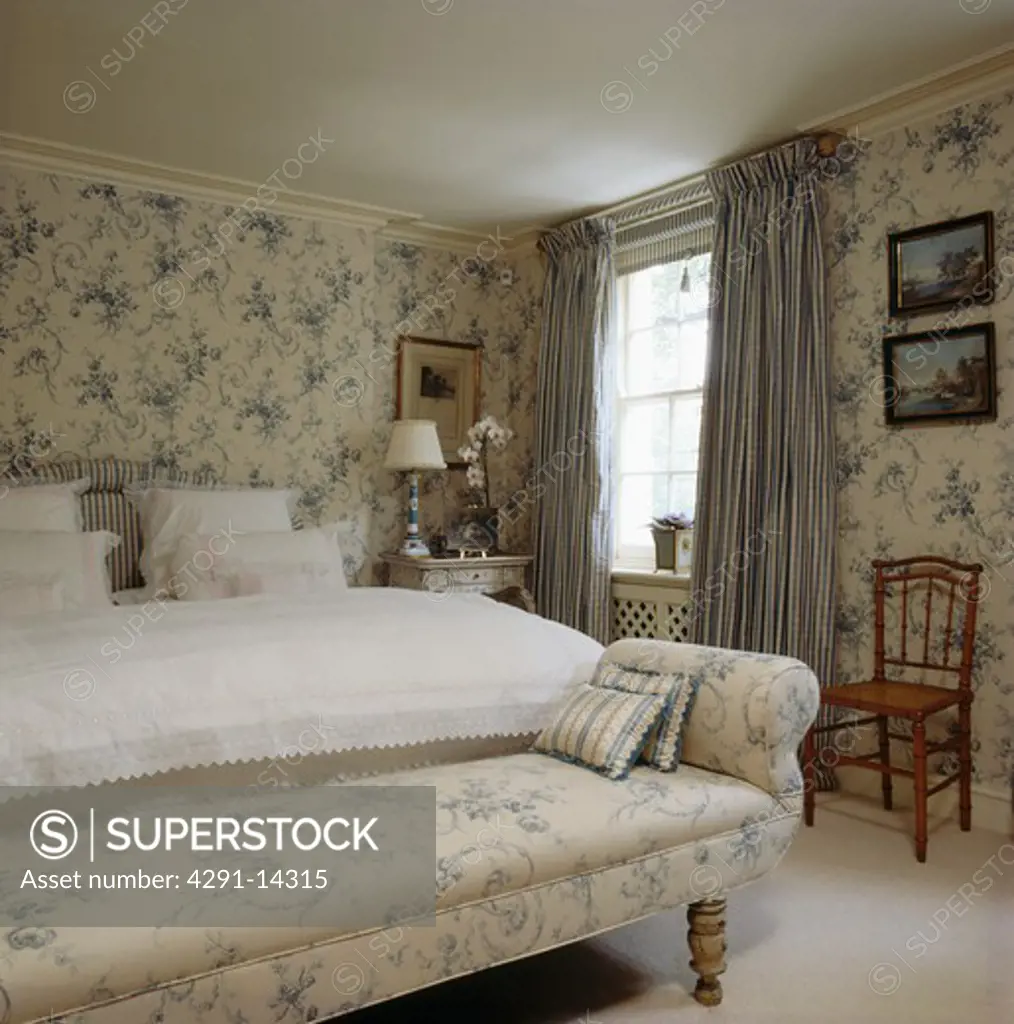 Blue floral chaiselongue and wallpaper inbedroom with blue checked curtains