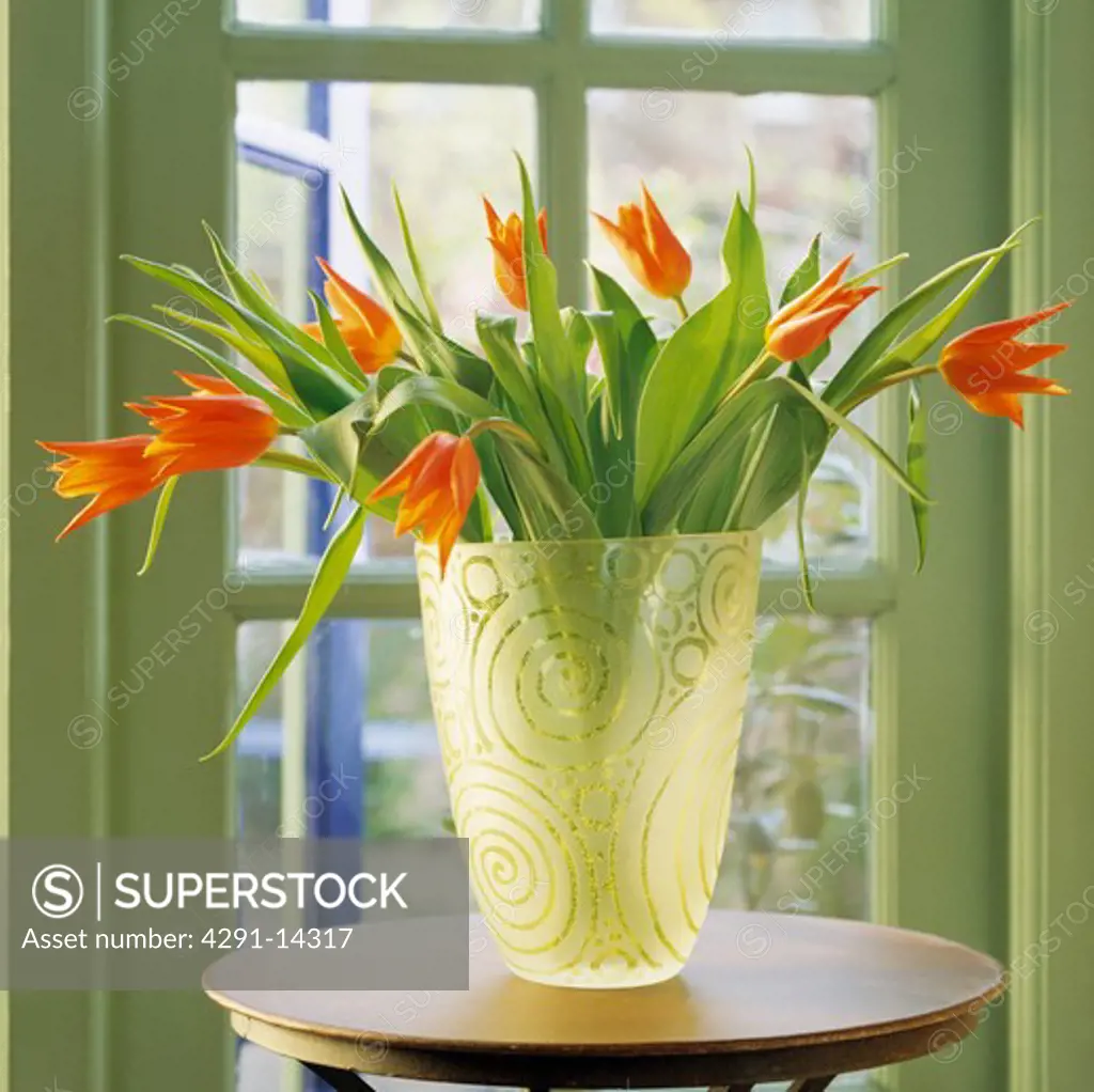 Close-up of orange tulips in engraved glass vase on small wooden table