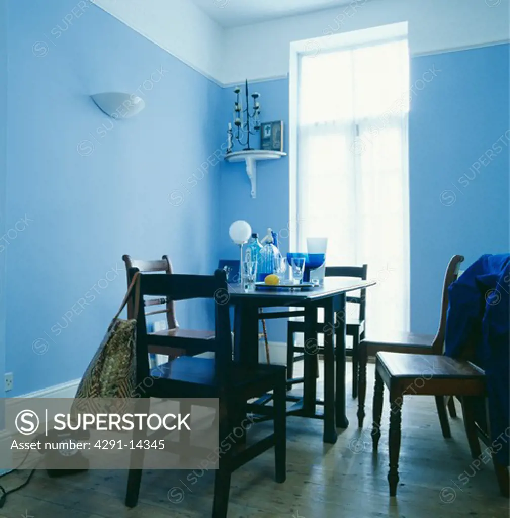 Plain wooden chairs and table in small pastel blue dining room with black fifties telephone on wooden floor