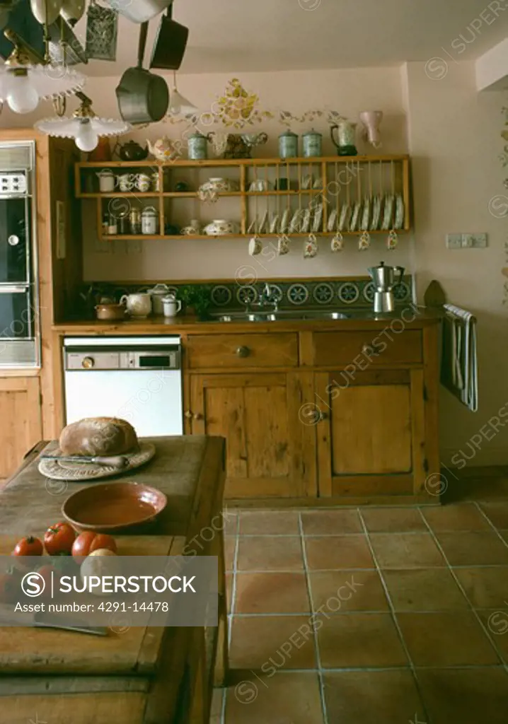 Vegetables on butcher's block in kitchen with terracotta tiled floor and plate rack with shelves above oven and sink