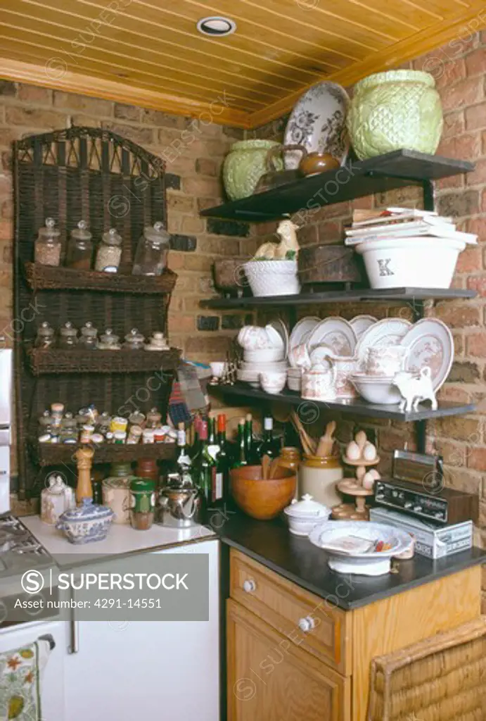 Crockery on shelves in corner of small kitchen with spice-rack above white fridge